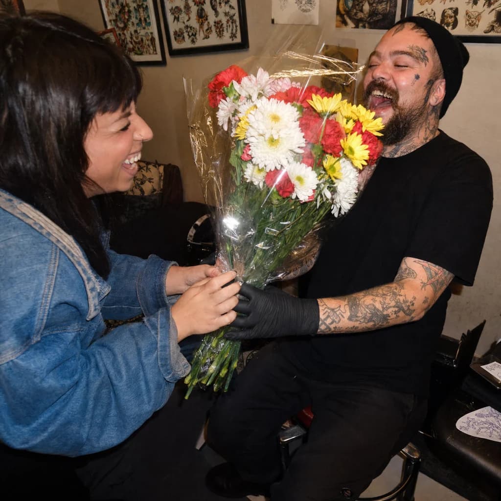 Client and tattoo artist laughing over a surprise bouquet